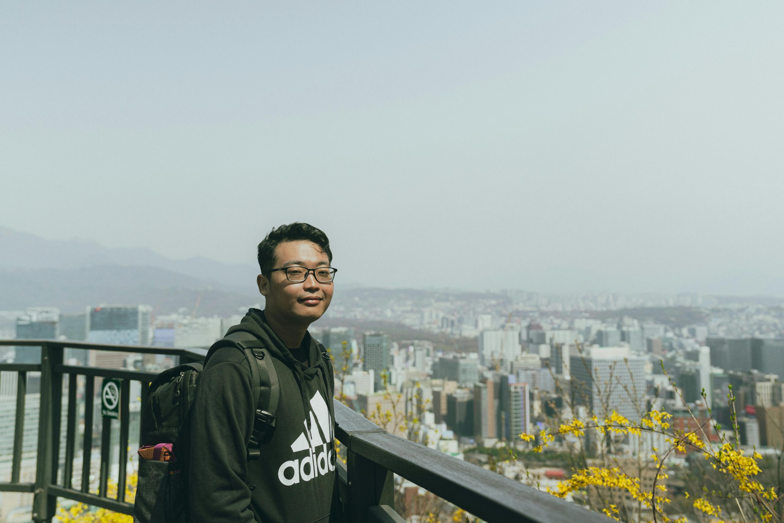 A man with a backpack enjoys a scenic view of Seoul, South Korea, surrounded by yellow blossoms.