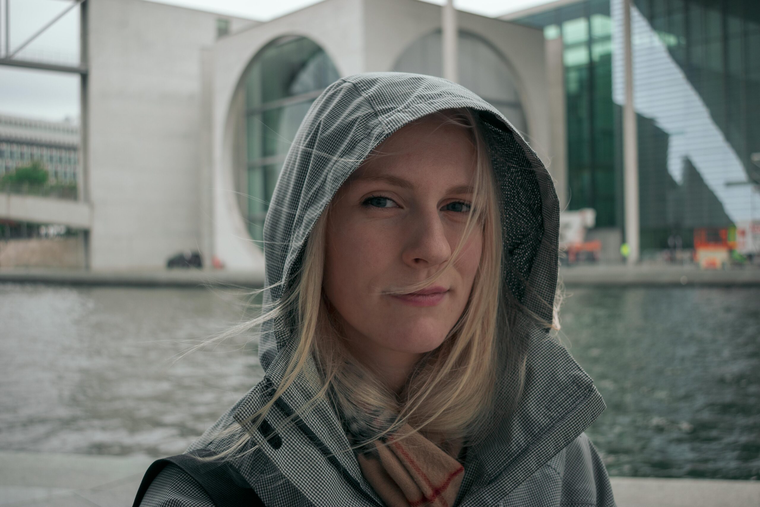 Blonde woman in a hooded jacket standing by the Spree River in Berlin.